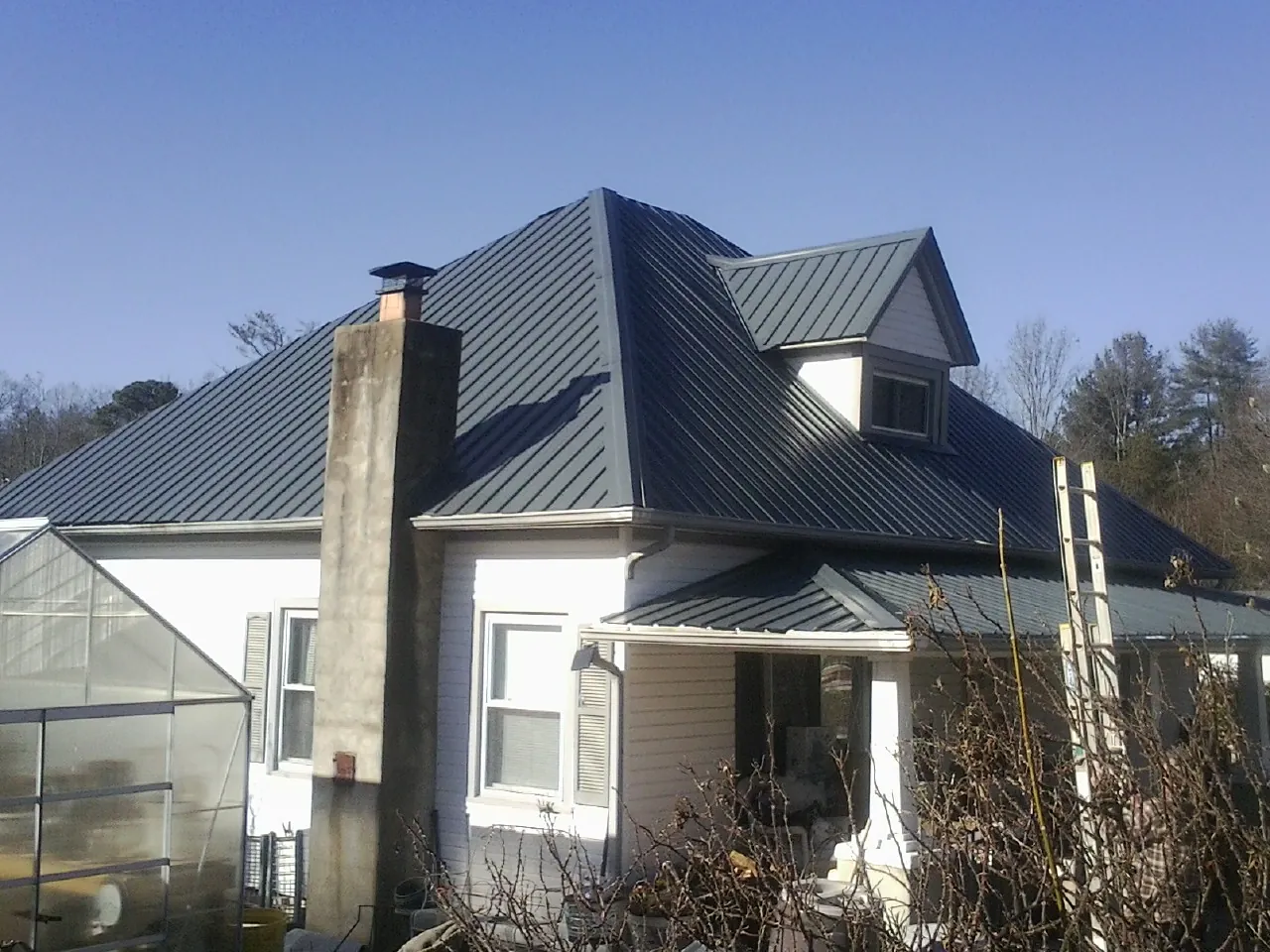 Dark blue standing seam metal roof on a white farmhouse with dormer — Slate & Tile Roof Repair by Roofing Brothers in Oviedo