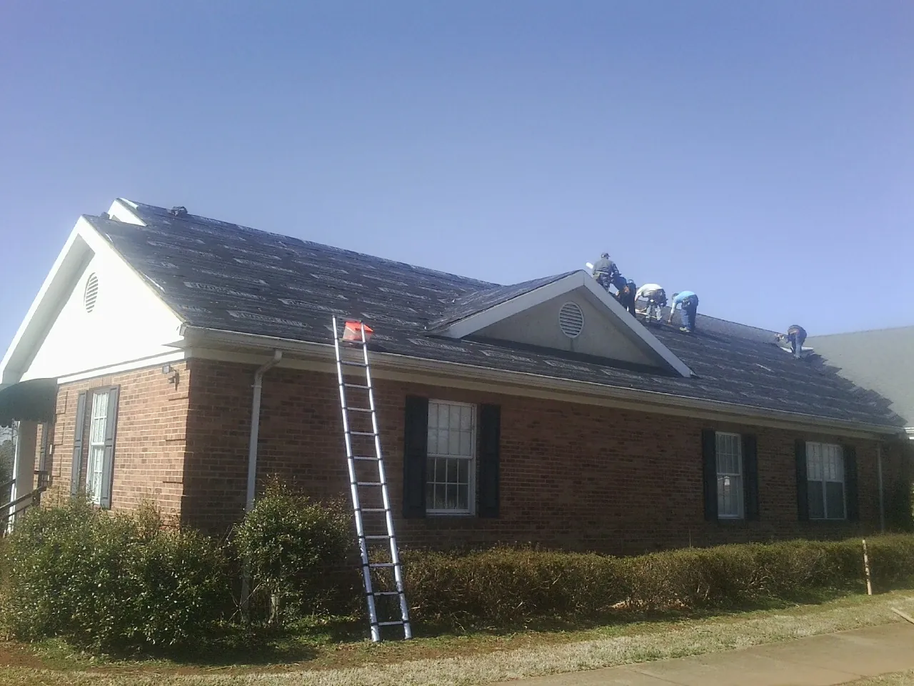 Crew tearing shingles off a brick ranch roof with a ladder set — Metal Roof Repair work by our crew in Oviedo