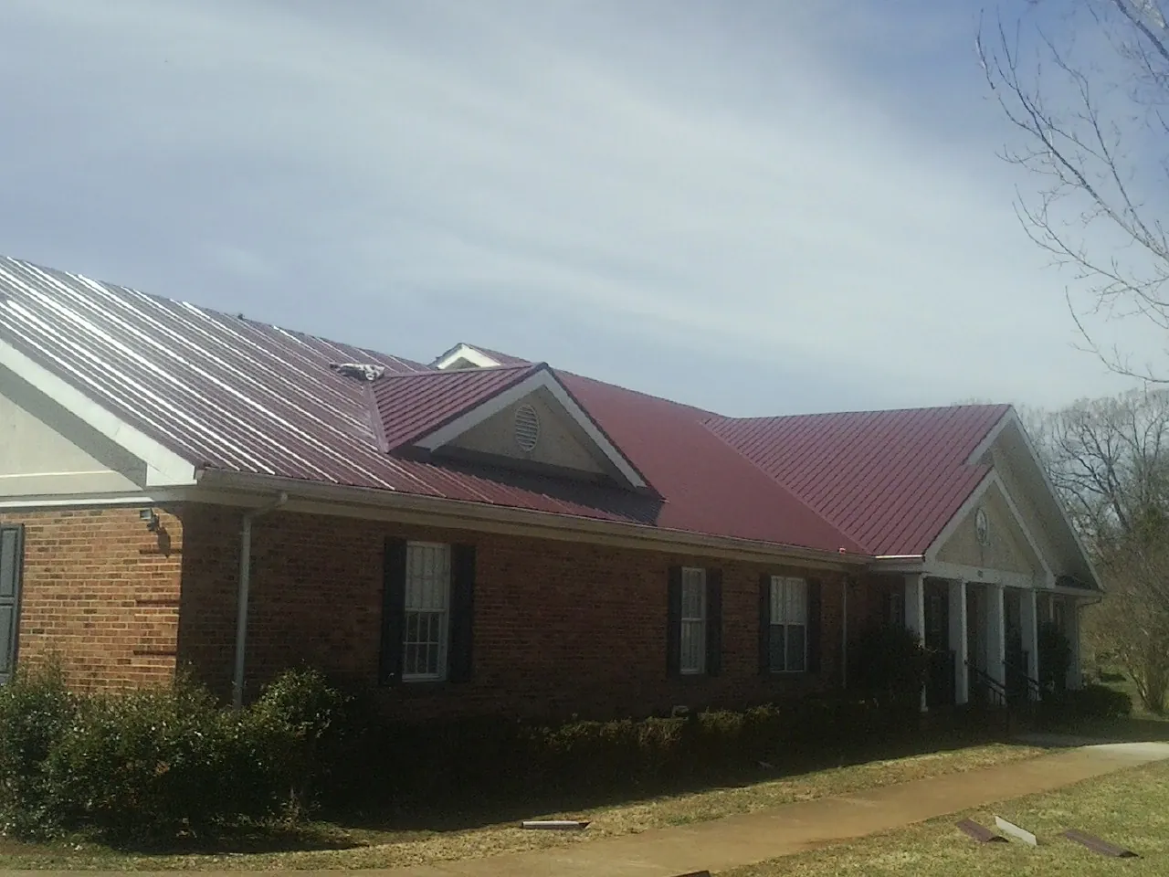 Red metal roof with gabled entries on a long brick building, from a Hail Damage Roof Repair job in Oviedo