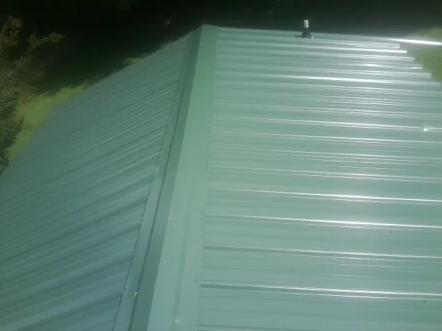 New green metal panels meeting at the ridge of a roof — Flat Roof Repair work by our crew in Oviedo