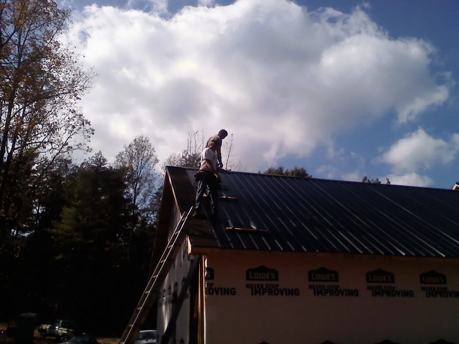 Roofer fastening dark metal panels high against a cloudy sky, from a Roof Inspection job in Oviedo