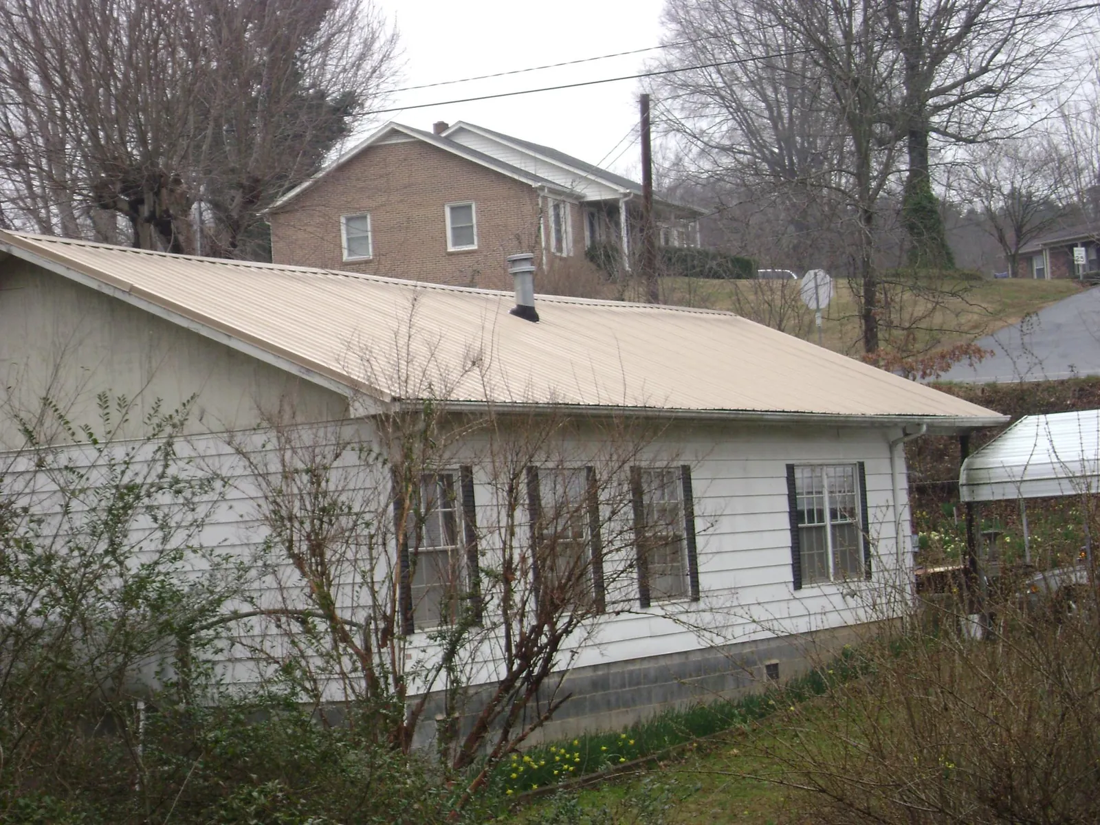 Tan metal roof on a white sided house set into a hillside — Commercial Roofing by Roofing Brothers in Oviedo